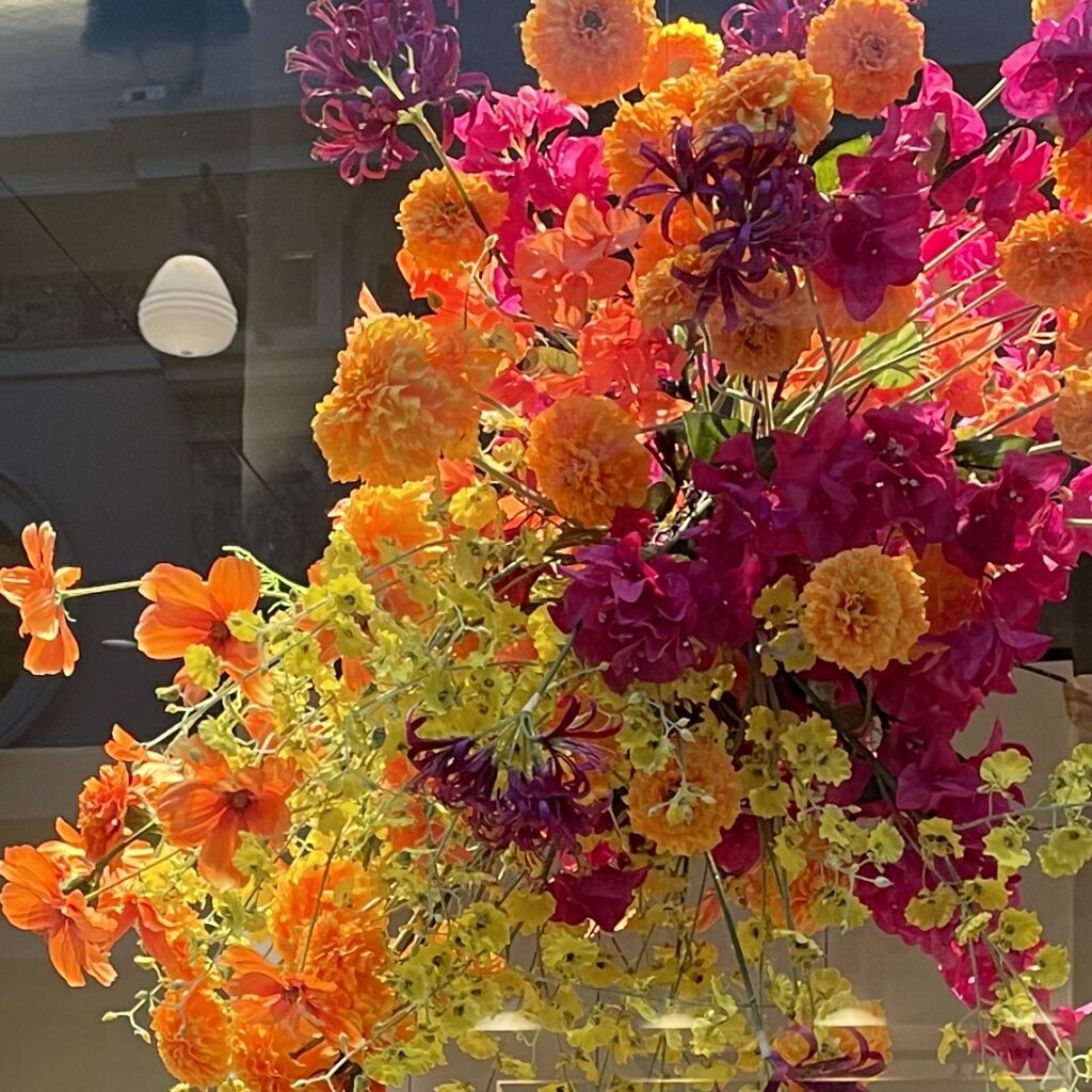 Installation florale cascadante en orange, jaune et fuchsia devant une vitrine